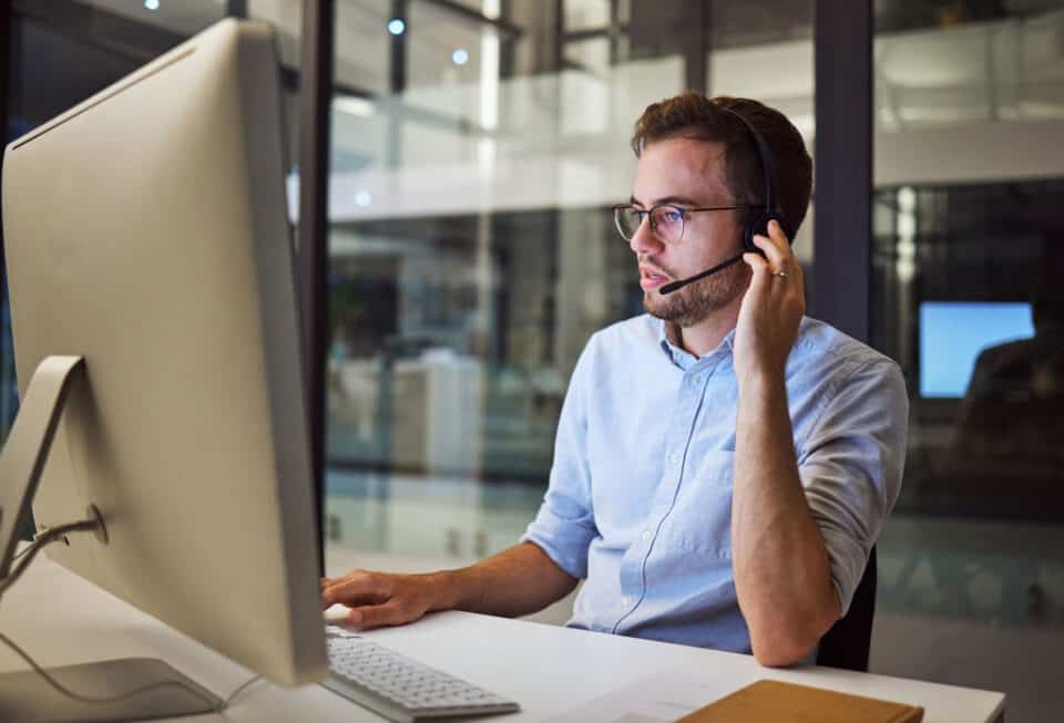 Call center support agent wearing headset working at modern office computer for IT services.